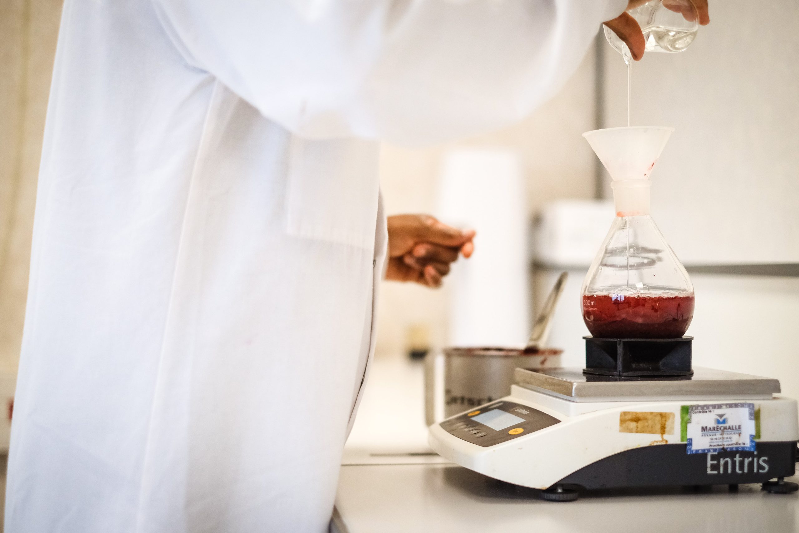 photo d'une aromaticienne dans un laboratoire qui verse une préparation aromatique dans un becher